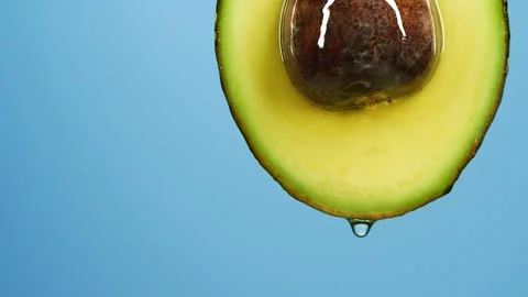 Slow motion of oil drop dripping from fresh avocado fruit over blue background Stock Footage 149234052