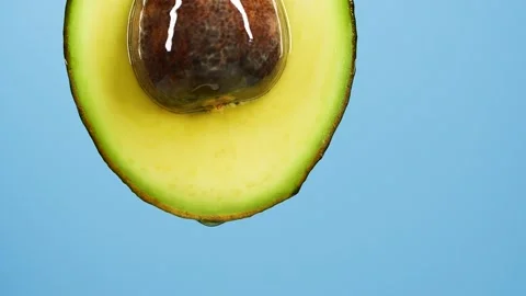 Slow motion of oil drop dripping from fresh avocado fruit over blue background Stock Footage 151497762