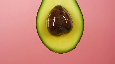 Slow motion of oil drop dripping from fresh avocado fruit over pink background Stock Footage 153571655