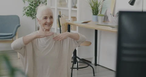 Slow motion of old lady working out and watching sports program on TV in living Stock Footage 237313687