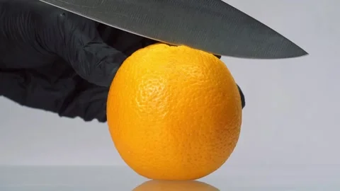 Slow motion orange cut. Man in black gloves slice orange fruit with big knife on Stock Footage 150771778