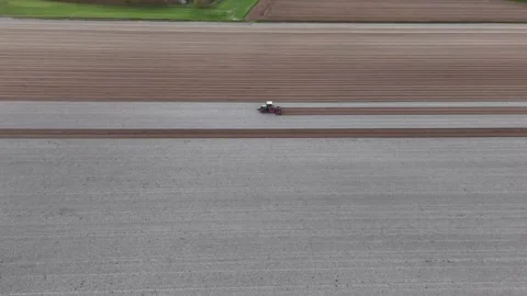 Slow-motion overhead drone of tractor smoothing earthen stripes across vast Stock Footage 308443399