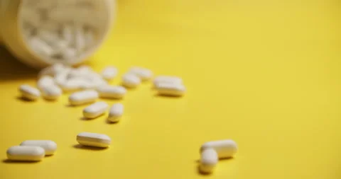Slow Motion Overhead View of Scattering White Pills on Yellow Stock Footage 307858852
