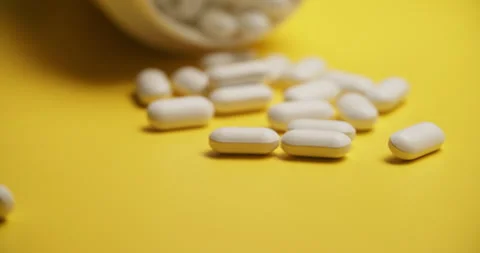 Slow Motion Overhead View of Scattering White Pills on Yellow 動画素材 307861487