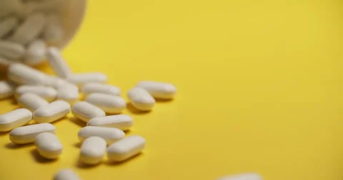 Slow Motion Overhead View of Scattering White Pills on Yellow Stock Footage 307861610
