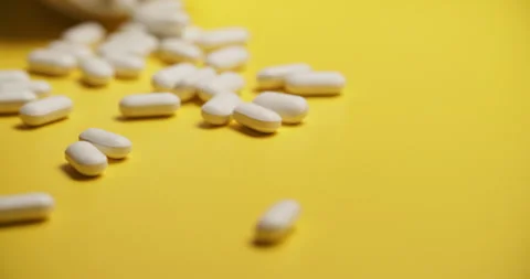 Slow Motion Overhead View of Scattering White Pills on Yellow 動画素材 307861736
