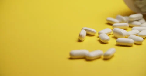 Slow Motion Overhead View of Scattering White Pills on Yellow Vídeos de archivo 307861787