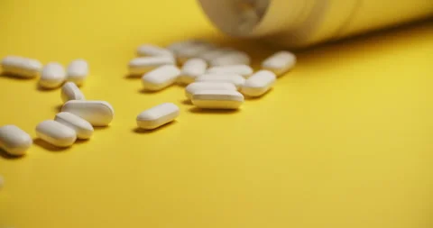 Slow Motion Overhead View of Scattering White Pills on Yellow Vídeos de archivo 307861932