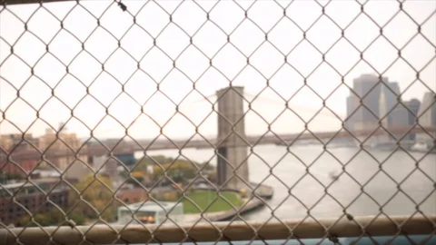 Slow motion pan of the Brooklyn Bridge and Manhattan skyline through chain fence Stock Footage 98646144