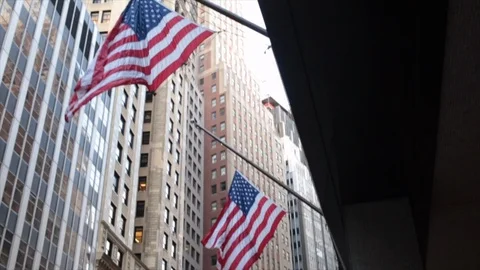 Slow motion pan down of United States flags flying against backdrop of skyscrape Stock Footage 98632449