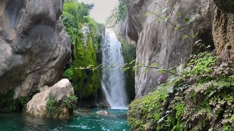 Slow motion pan out of a waterfall among rock walls and wild vegetation Stock Footage 194484812