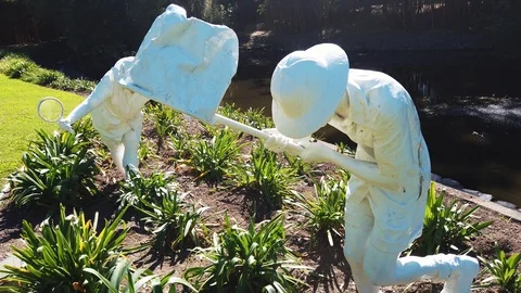 Slow motion pan reveal of two white statues by pond Video stock 108968736