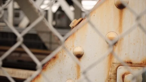 Slow motion pan up through chain fence looking at subway passing over the Manhat Stock Footage 98646207