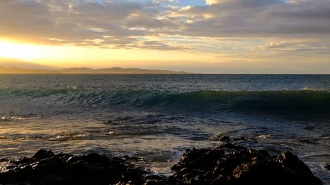 Slow motion pan of wave breaking along rocky shore at sunrise Vidéo 107877524