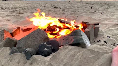 Slow motion parallax of beach campfire, revealing feet of woman enjoying Stock Footage 203939838