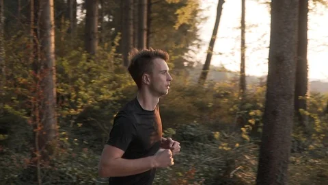 Slow motion pass by of young man athlete running through forest, slow motion Stock Footage 129611549