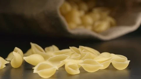 SLOW MOTION: Pasta (conchiglie) fall near a lying cloth bag Stockbeeldmateriaal 72495984