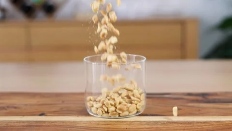 Slow Motion Peanuts Dropping into Full Glass Cup Stock Footage 253392860