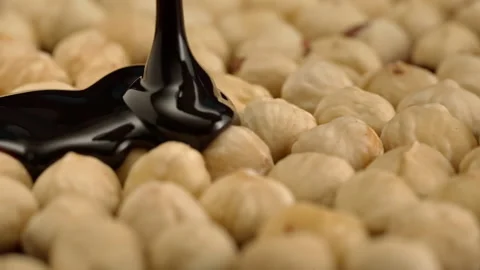 Slow motion peeled hazelnuts sprinkled with chocolate on a black background Stock Footage 148222124