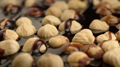 Slow motion peeled hazelnuts sprinkled with chocolate on a black background Stock Footage 148222210
