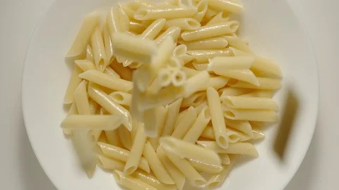 SLOW MOTION: Penne pasta falling into a white plate - Top View Stock Footage 100631857