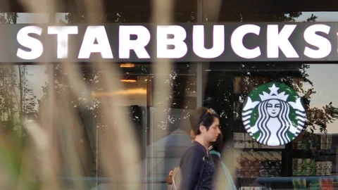 Slow motion of people walking through starbucks store with blurry leaves blowing Stock Footage 80049737