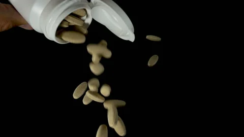 Slow motion of pills falling from a white jar on a black Stock Footage 113355000