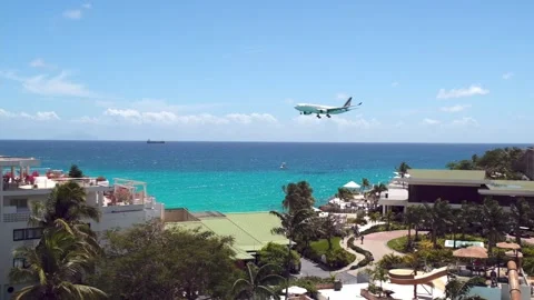 Slow motion plane flies low altitude above coastal hotel next to Maho resort Stock Footage 233233843