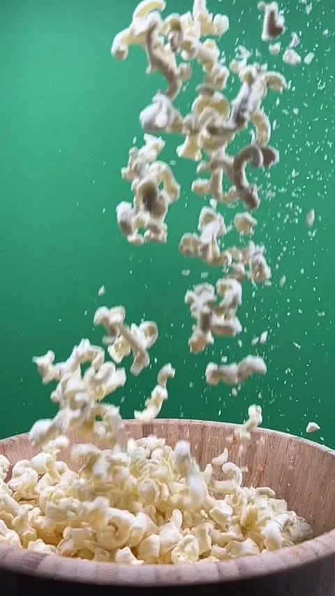 Slow motion of popcorn falling into a wooden bowl, vertical view Stock Footage 345154940