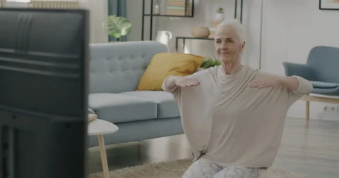 Slow motion portrait of beautiful elderly lady exercising and watching TV in Stock Footage 237953412