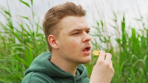 Slow motion portrait close up of a Young man who eats tortilla chips outside Stock Footage 91230861