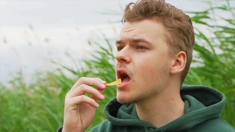 Slow motion portrait close up of a Young man who eats tortilla chips outside Stock Footage 91230877