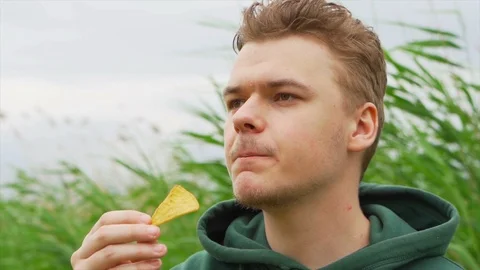 Slow motion portrait close up of Young man who eats tortilla chips outside Stock Footage 91230939