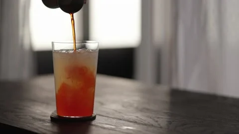 Slow motion pour orange syrup in lemonade in tumbler glass with crushed ice on Stock Footage 173767389