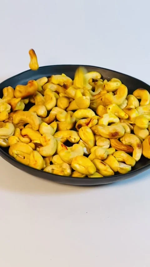 Slow motion of pouring cashew nuts into black plate, close-up Stock Footage 336471112