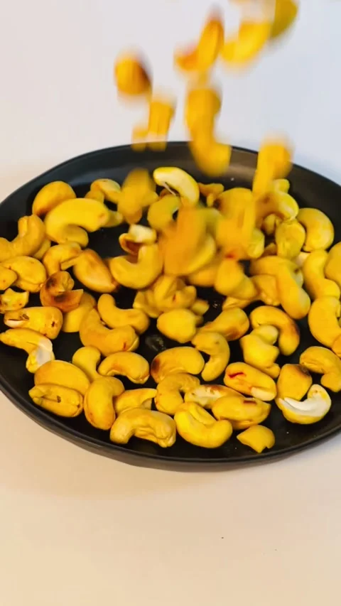 Slow motion of pouring cashew nuts into black plate, close-up Stock Footage 336471114