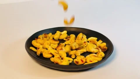 Slow motion of pouring cashew nuts into black plate, close-up Stock Footage 336471116
