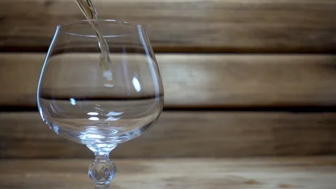 Slow motion pouring a cognac or brandy into glass on wooden Stock Footage 85424367