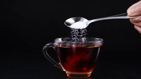 Slow motion pouring sugar with a spoon into a glass cup of black tea Stock Footage 332870735