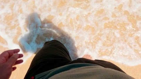Slow motion POV high angle of man walking barefoot on sandy beach shoreline Stock Footage 345389021