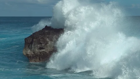 SLOW MOTION: Powerful ocean wave splashes across a big rock in the middle of sea Stock Footage
