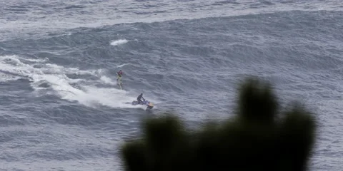 Slow motion of professional surfer behind jet ski wake surfing across ocean Stock Footage 163339904