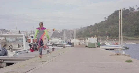 Slow motion of professional surfer Maya Gabiera walks alongside of harbour Stock Footage 157134055