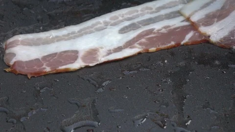 Slow motion of putting sliced bacon on dark gray fry pan close up. Stock Footage 99851600