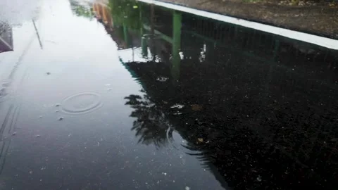 Slow motion rain can be seen as raindrops hitting water on the ground. 動画素材 289679612
