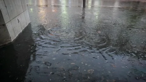 Slow motion rain can be seen as raindrops hitting water on the ground. 動画素材 289679631