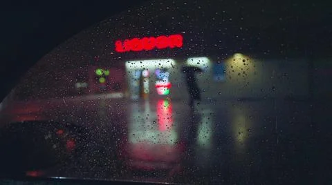 Slow motion rain drops falling into puddle on asphalt at night. Big modern city Stock Photos