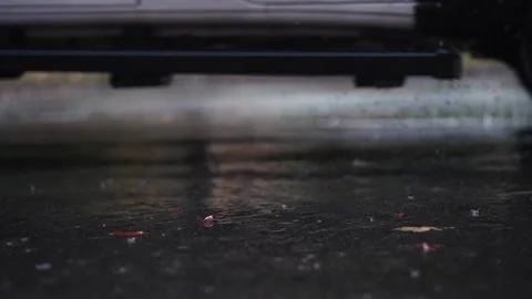 Slow-motion raindrops hit the black concrete pavement with a car driving past in Vídeo Stock 292836998