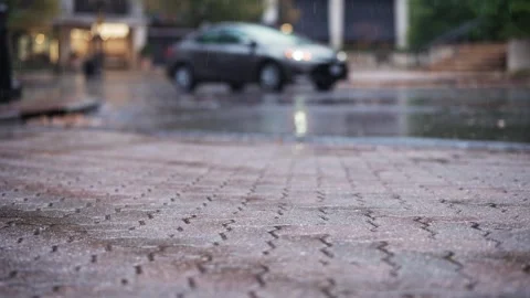 Slow-motion raindrops hit the concrete pavement with a dark grey car driving in Stock-Footage 292836621