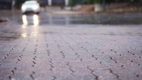 Slow-motion raindrops hit the concrete pavement with a white SUV driving in the Stock Footage 292836629